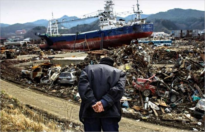 Starší Japonec se dívá z kopce na město Išinomaki zničené tsunami. 2011 g